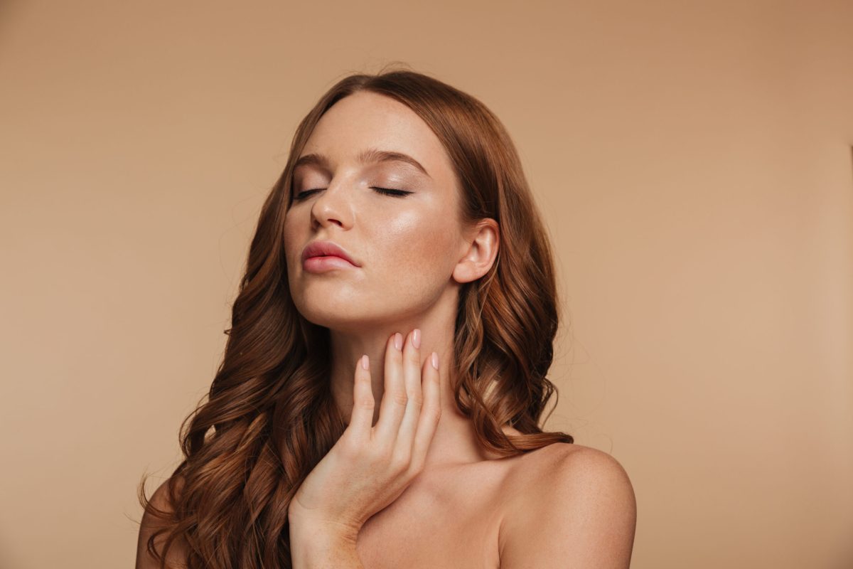 Beauty portrait of sensual ginger woman with long hair posing with closed eyes over cream background